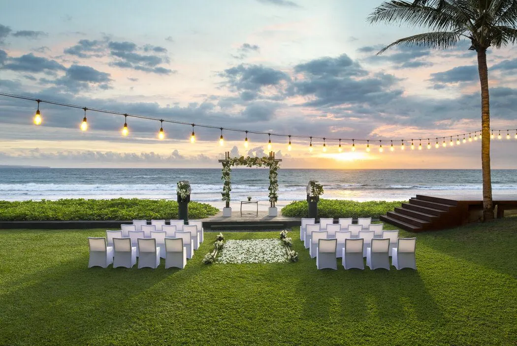 Beachfront ceremony arch at dusk under a string of Edison bulbs and a lone palm