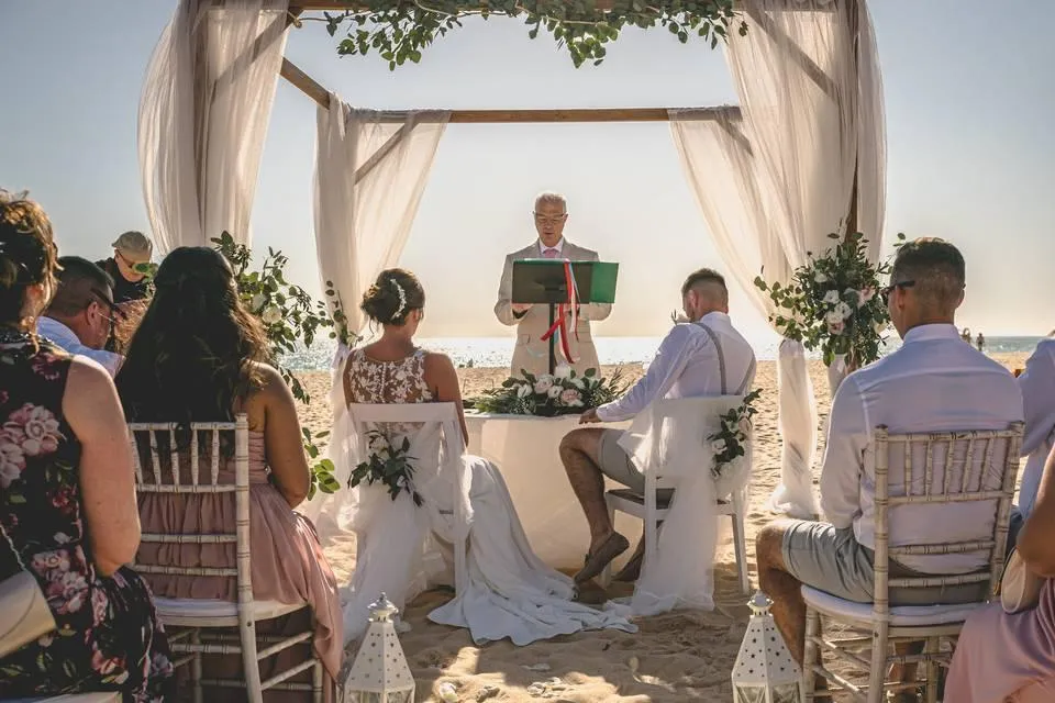 Beach ceremony under a wooden canopy draped with linen and eucalyptus