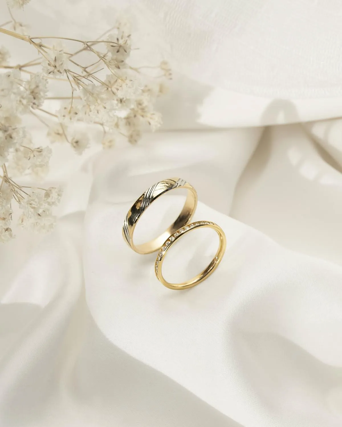 His and hers wedding bands resting on ivory silk beside dried gypsophila