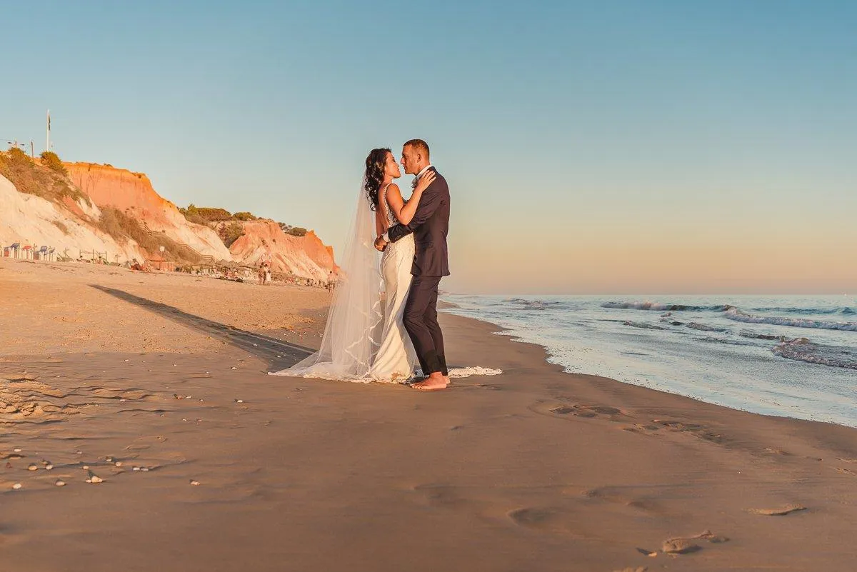 Bride and groom facing each other on the sand at golden hour with the waves behind them
