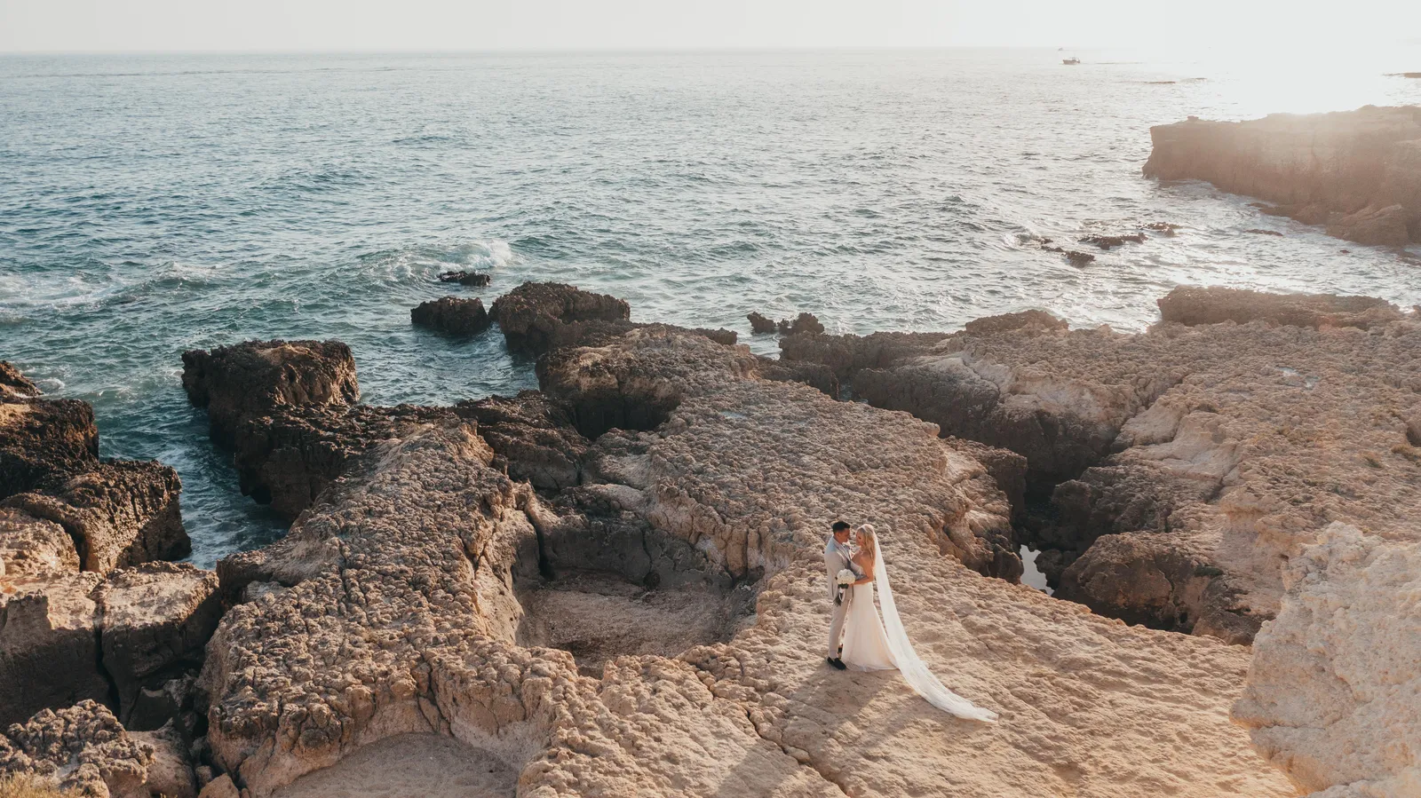 Distant view of a couple embracing on a sculpted rock plateau above the Atlantic