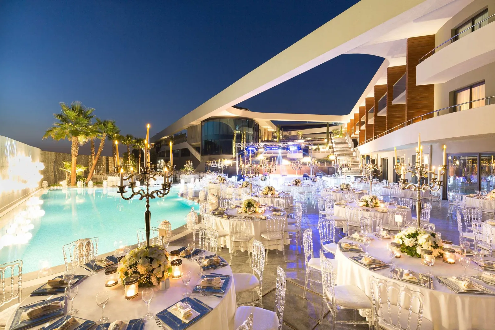 Poolside reception at blue hour lit by silver candelabras and dozens of tapers